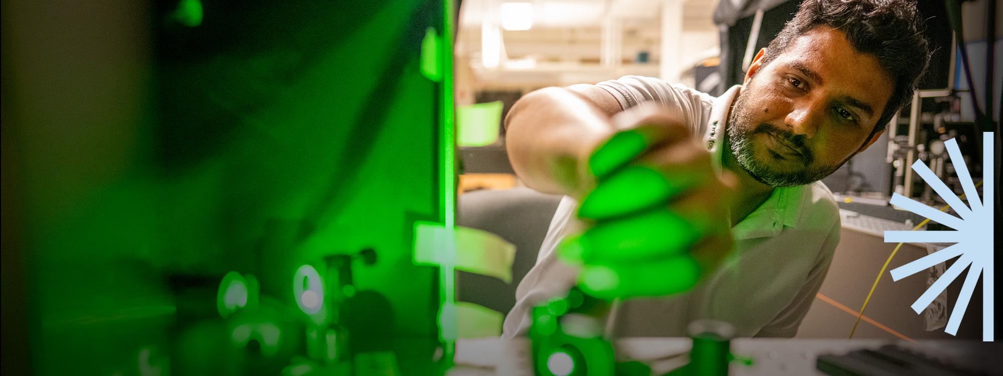A man is performing research in the physics lab. His hand is reaching towards you with a green glow on his hand.